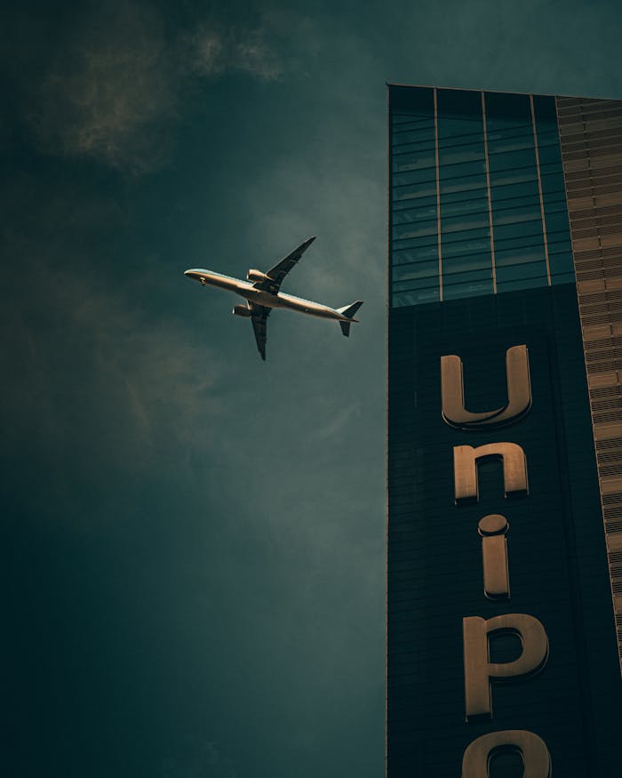 digital Low angle view of an airplane flying near a skyscraper with a dramatic sky.